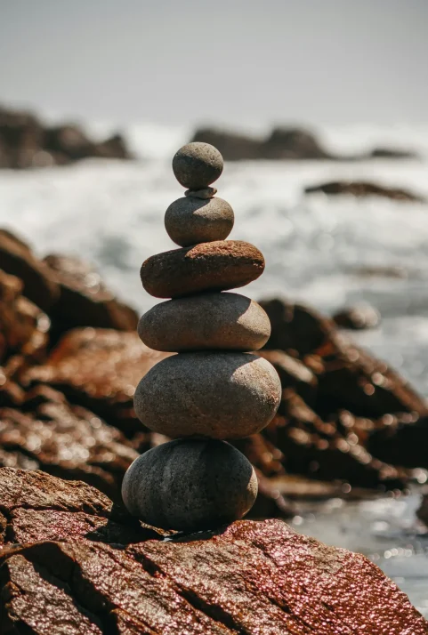 jordyn-montague-ZpkZulvFhvQ-unsplash Stacked stones balanced on a beach with waves in the background.